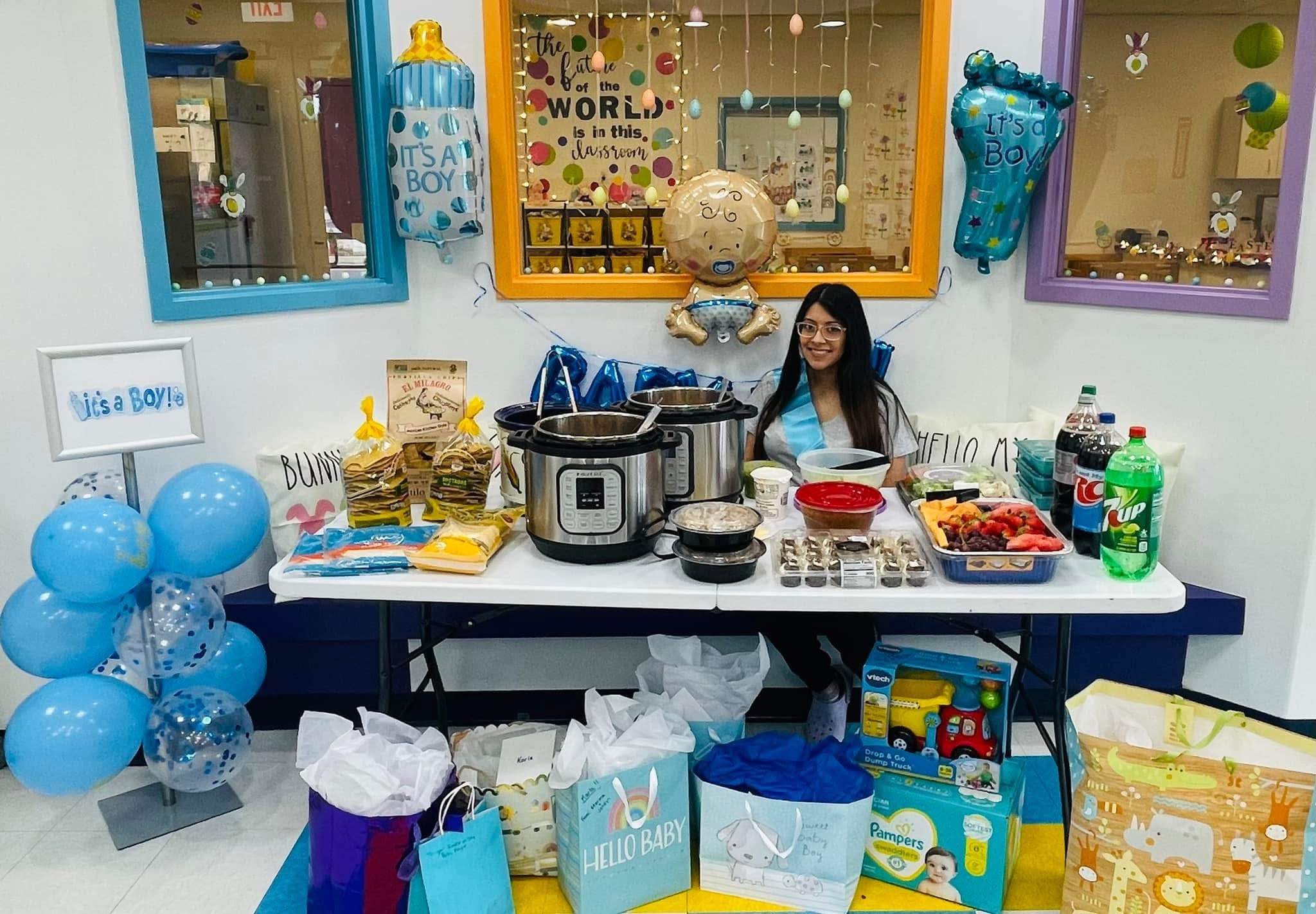 A team member standing behind the food and gift table, surrounded by blue baby shower decorations
